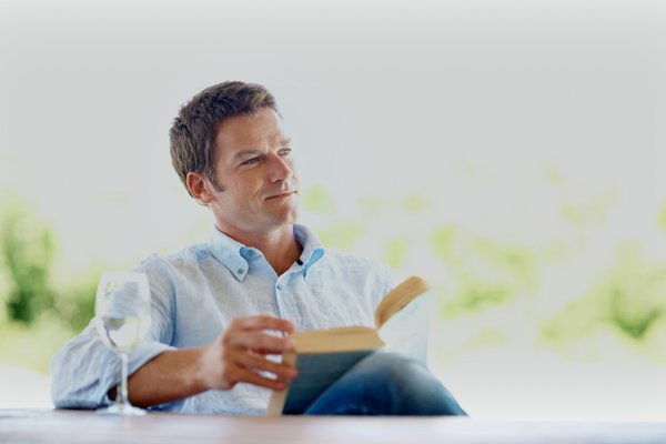 Guy reading a book with a wine glass next to him